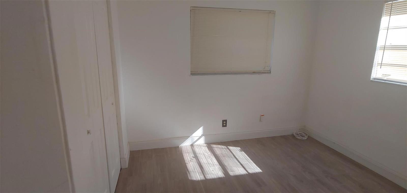 An empty bedroom features white walls, light wood-look flooring, a closet, and two windows — 3860 NW 8th Place, Lauderhill FL 33311, LAUDERHILL, FL