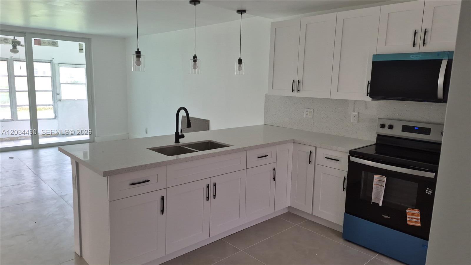 A modern kitchen features white cabinets, quartz countertops, a black faucet, and stainless steel appliances — 6050 NW 64th Ave # 105, Tamarac FL 33319, TAMARAC, FL
