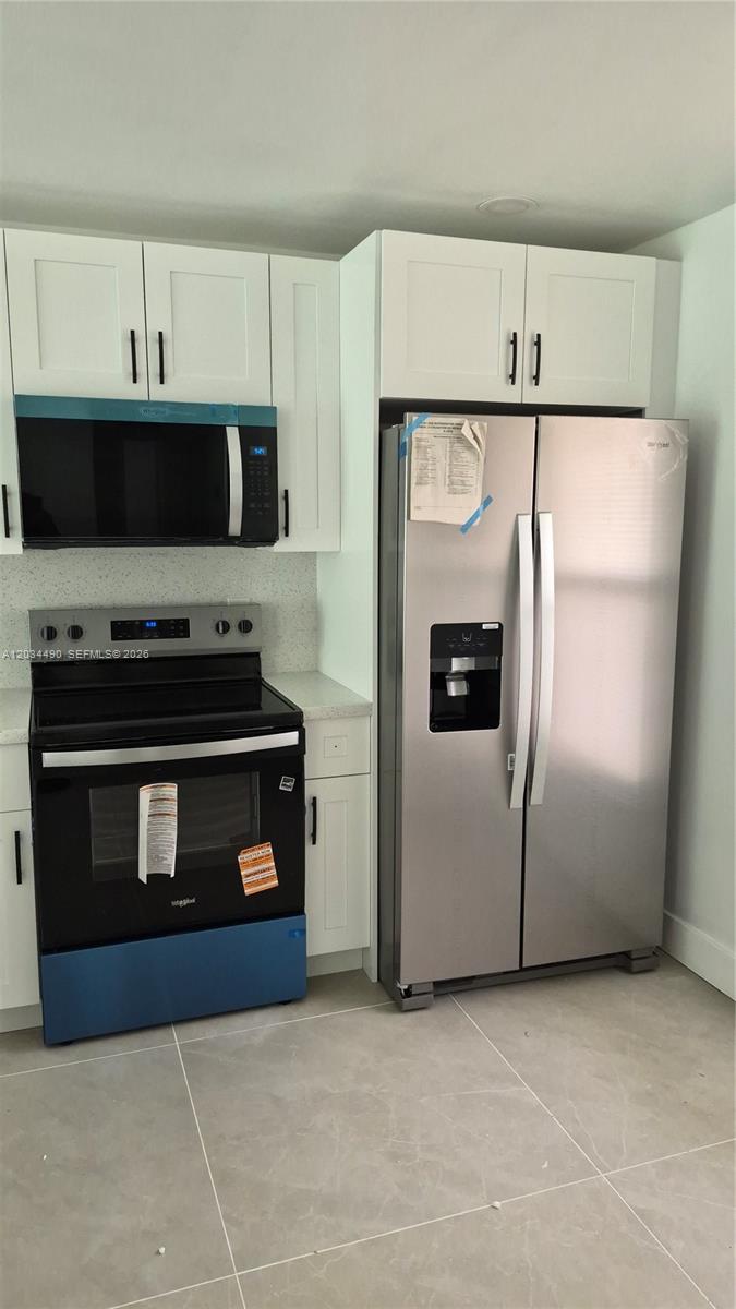 A kitchen features white cabinets, stainless steel appliances, and light-colored tile flooring — 6050 NW 64th Ave # 105, Tamarac FL 33319, TAMARAC, FL