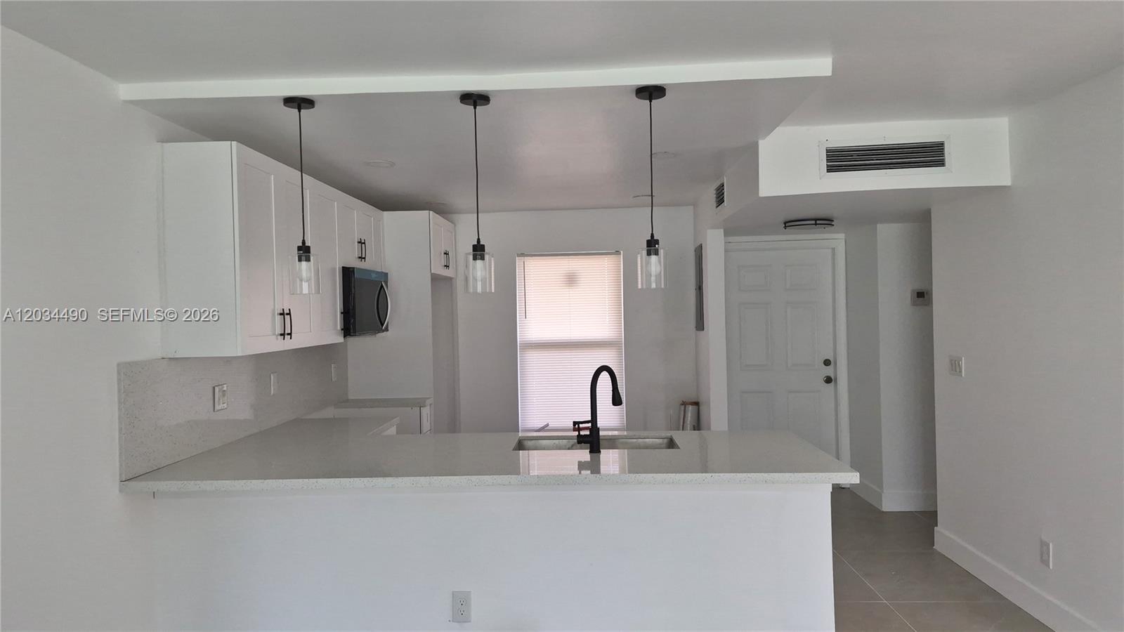A modern kitchen features white cabinets, quartz countertops, a breakfast bar, and three pendant lights — 6050 NW 64th Ave # 105, Tamarac FL 33319, TAMARAC, FL