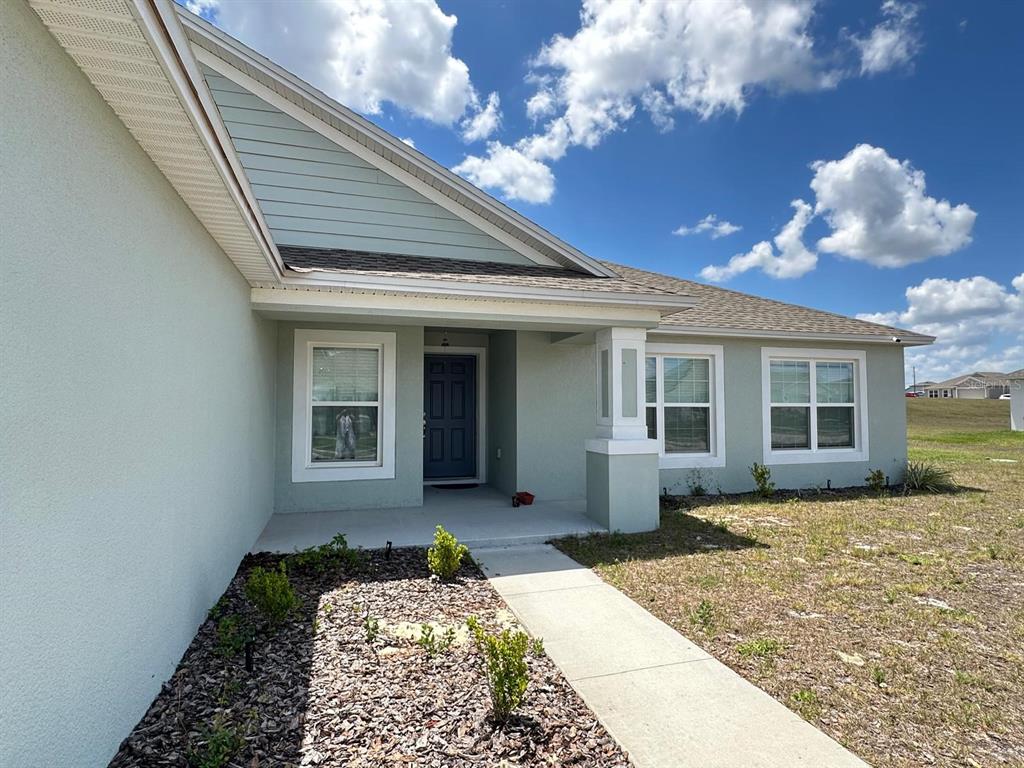 A light green house exterior features a covered entryway, a dark door, and a walkway — 1116 CALOOSA RIDGE WAY, BABSON PARK, FL