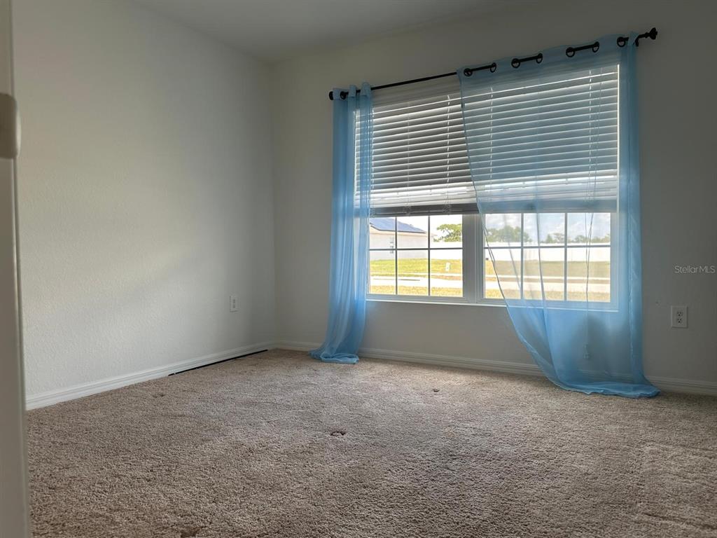 An empty bedroom features beige carpeting, white walls, and a window with blue curtains — 1116 CALOOSA RIDGE WAY, BABSON PARK, FL