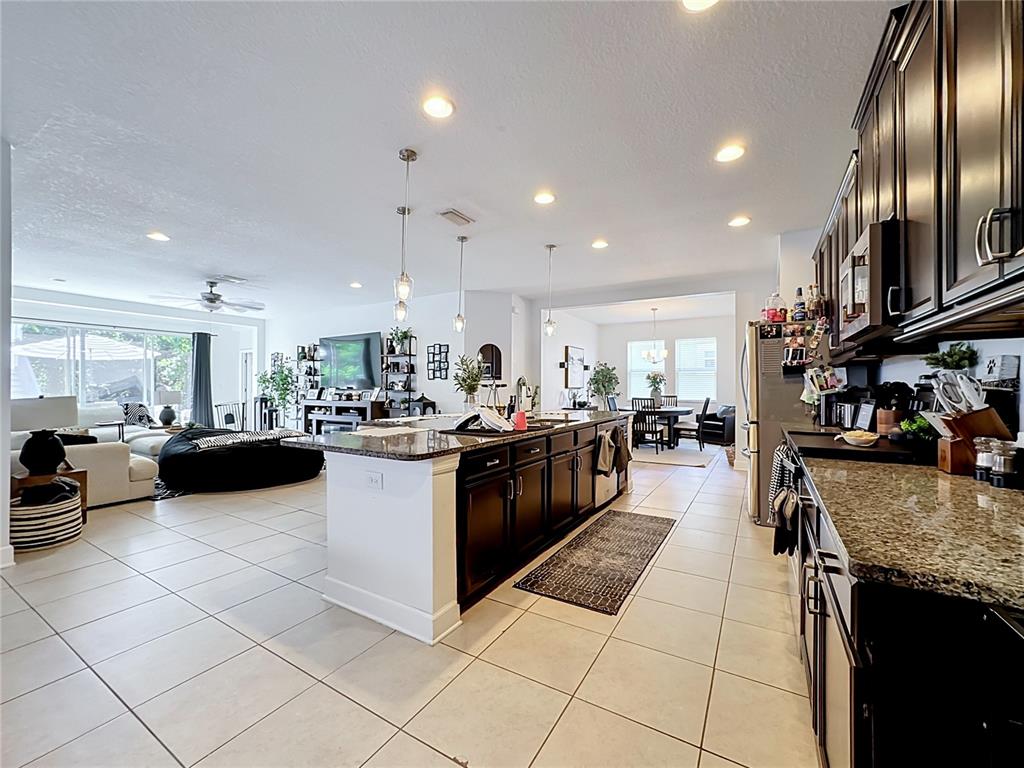 A kitchen with dark wood cabinets and granite countertops opens into a living area — 10457 WATERSTONE DRIVE, RIVERVIEW, FL