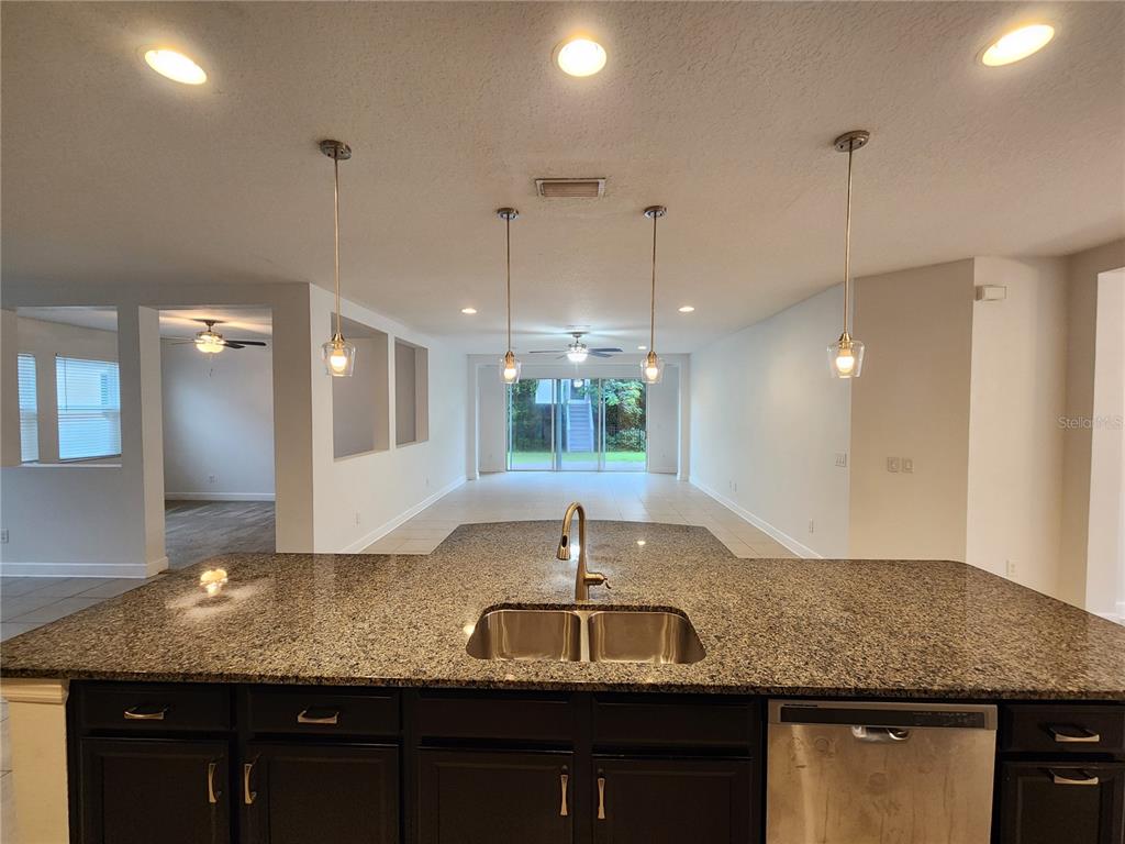 A kitchen island with a granite countertop and sink overlooks an open-concept living area — 10457 WATERSTONE DRIVE, RIVERVIEW, FL