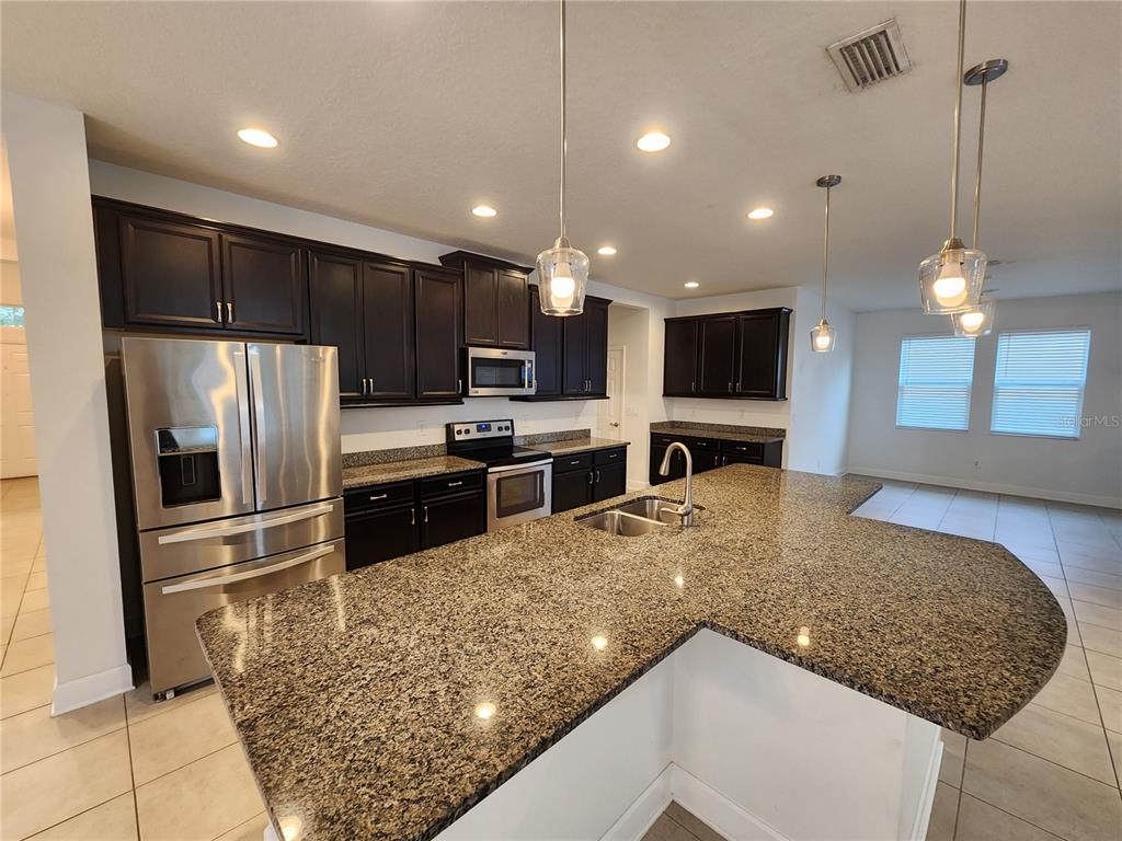 A kitchen features dark wood cabinets, granite countertops, stainless steel appliances, and a large island — 10457 WATERSTONE DRIVE, RIVERVIEW, FL