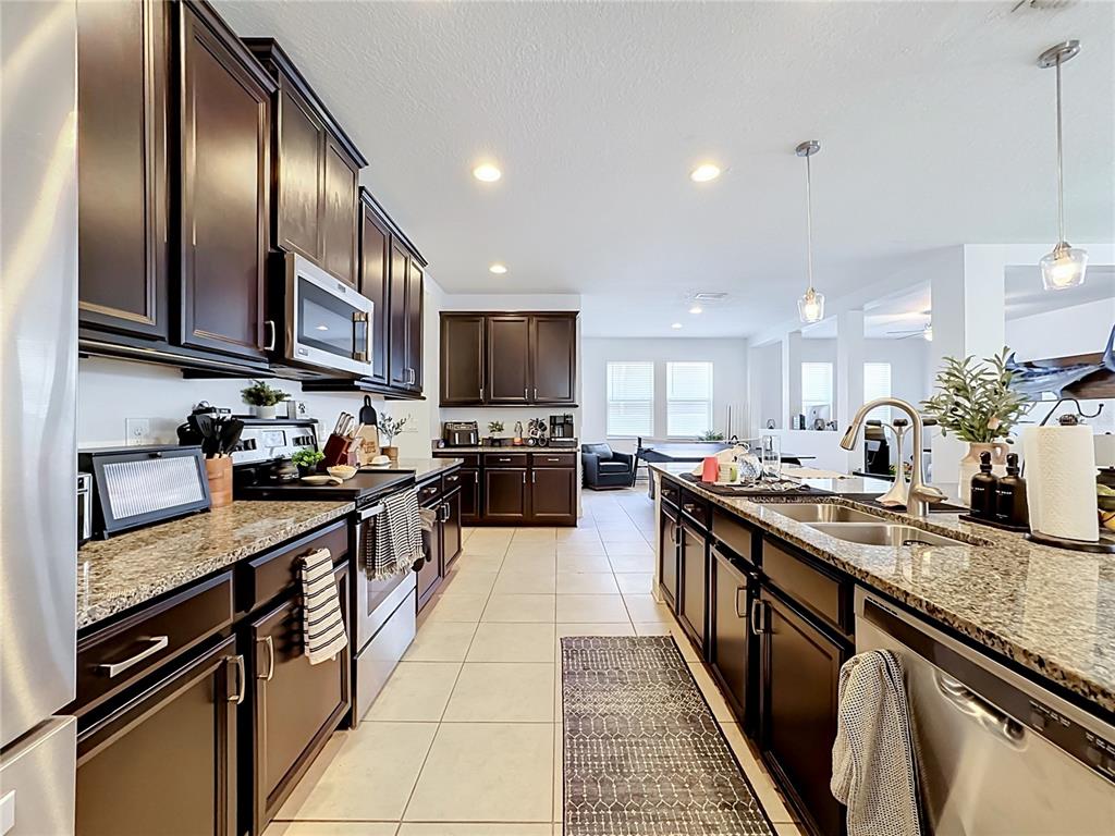 A kitchen features dark wood cabinets, granite countertops, stainless steel appliances, and tile flooring — 10457 WATERSTONE DRIVE, RIVERVIEW, FL