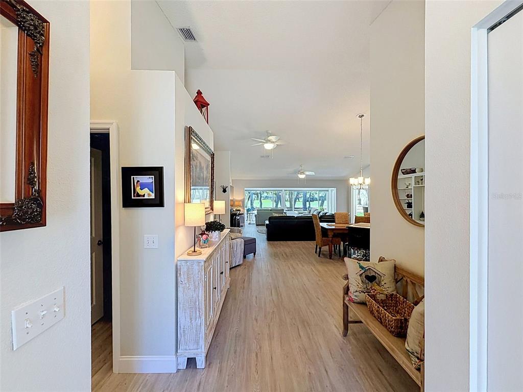 A view from a hallway looking into an open-concept living and dining area with wood-look flooring — 7442 WOODHOLLOW ROAD, SPRING HILL, FL