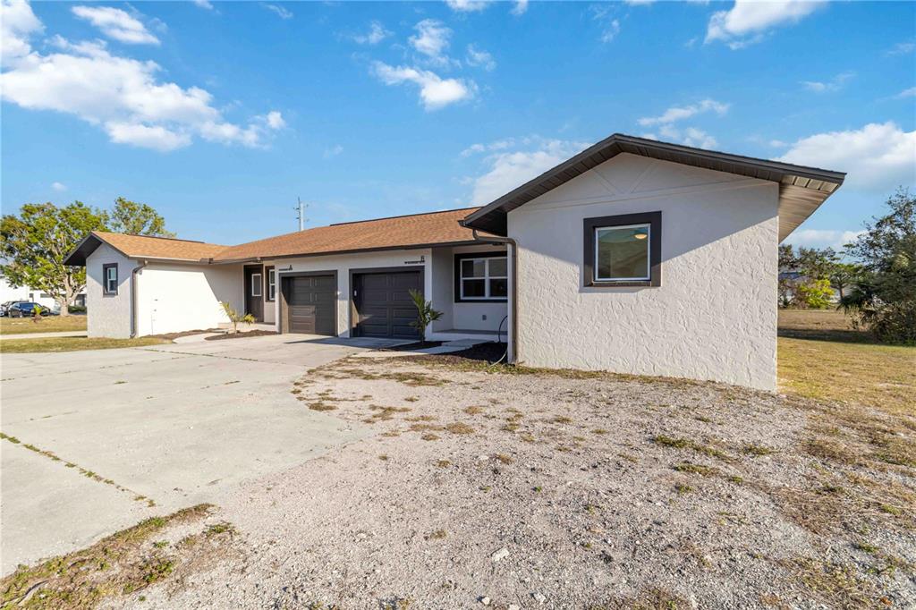 A single-story house with a white stucco exterior, two garage doors, and a gravel driveway — 49 BOUNDARY BOULEVARD UNIT B, ROTONDA WEST, FL