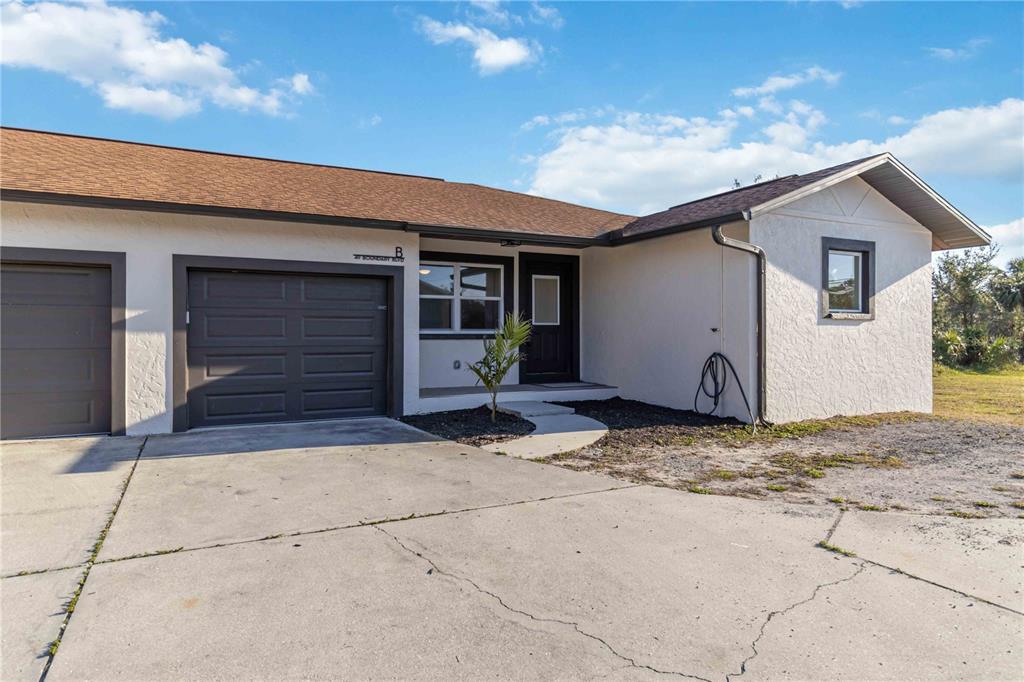 A single-story duplex with a white stucco exterior, brown roof, and attached garage — 49 BOUNDARY BOULEVARD UNIT B, ROTONDA WEST, FL