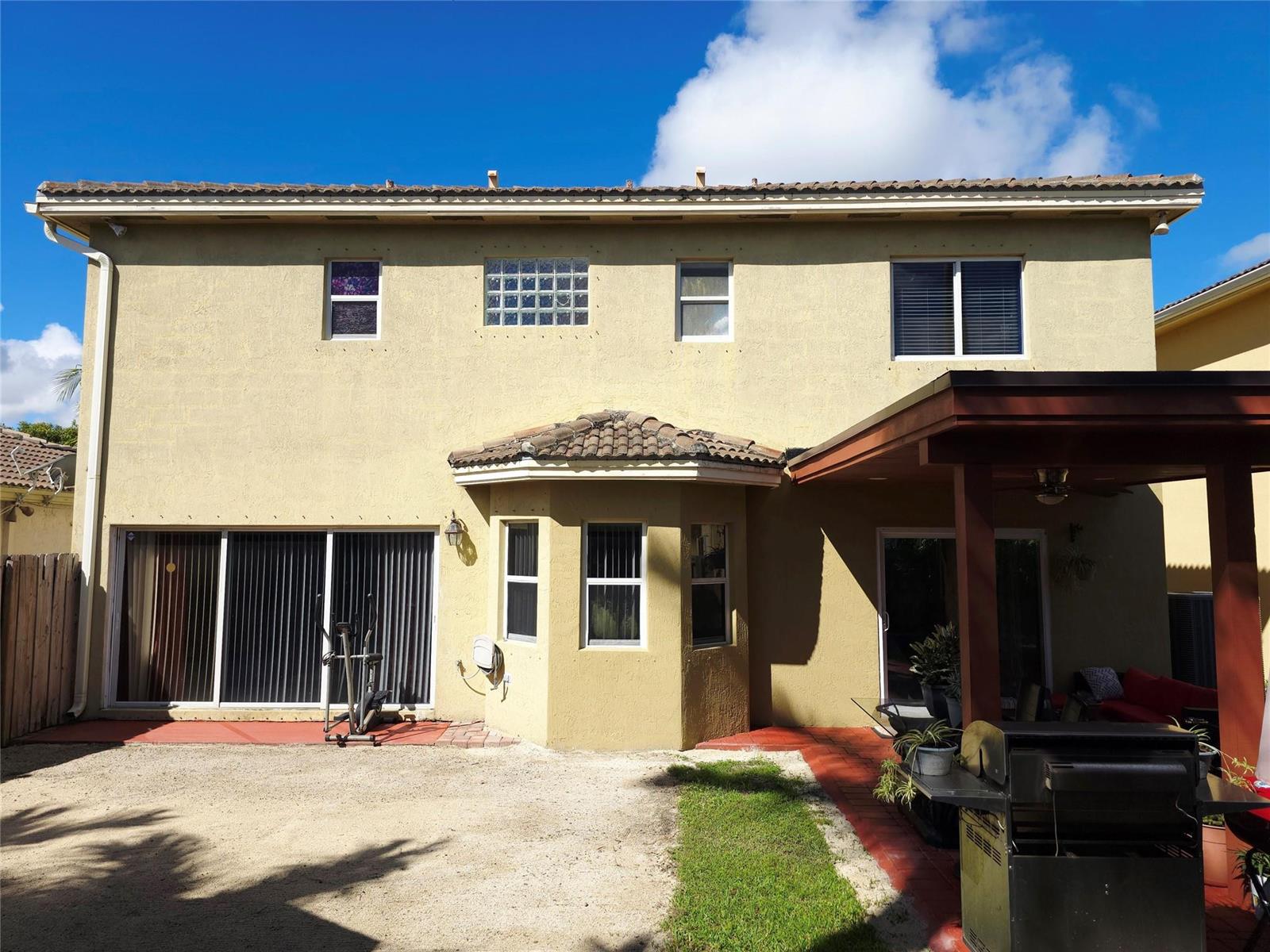 The rear exterior of a two-story stucco house features a patio, pergola, and bay window — 21053 SW 88th Place, Cutler Bay FL 33189, CUTLER BAY, FL