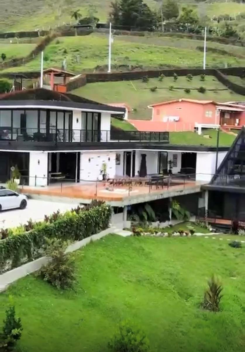 A modern two-story house with a large terrace sits on a grassy hillside — Los Altos Del Penol El Penol, FL