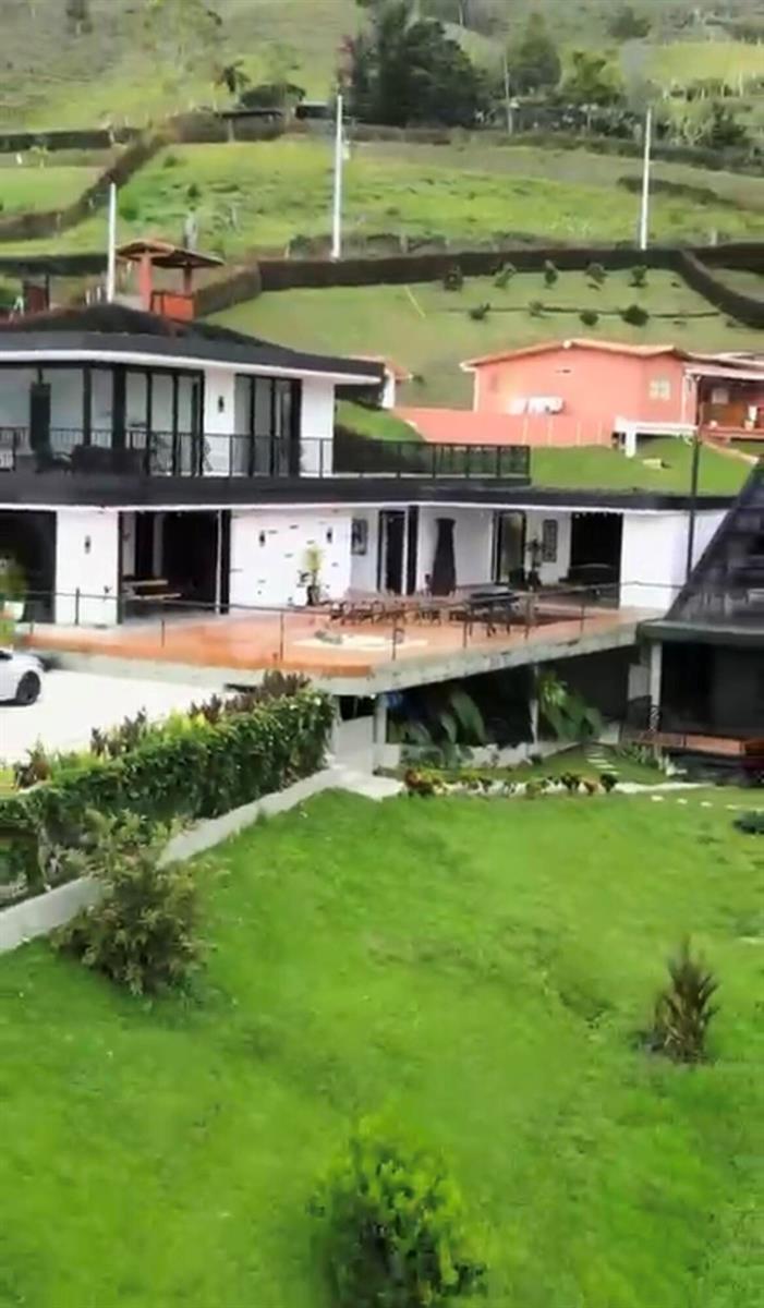 A modern two-story house with a large balcony overlooks a grassy lawn and hillside — Los Altos Del Penol El Penol, FL