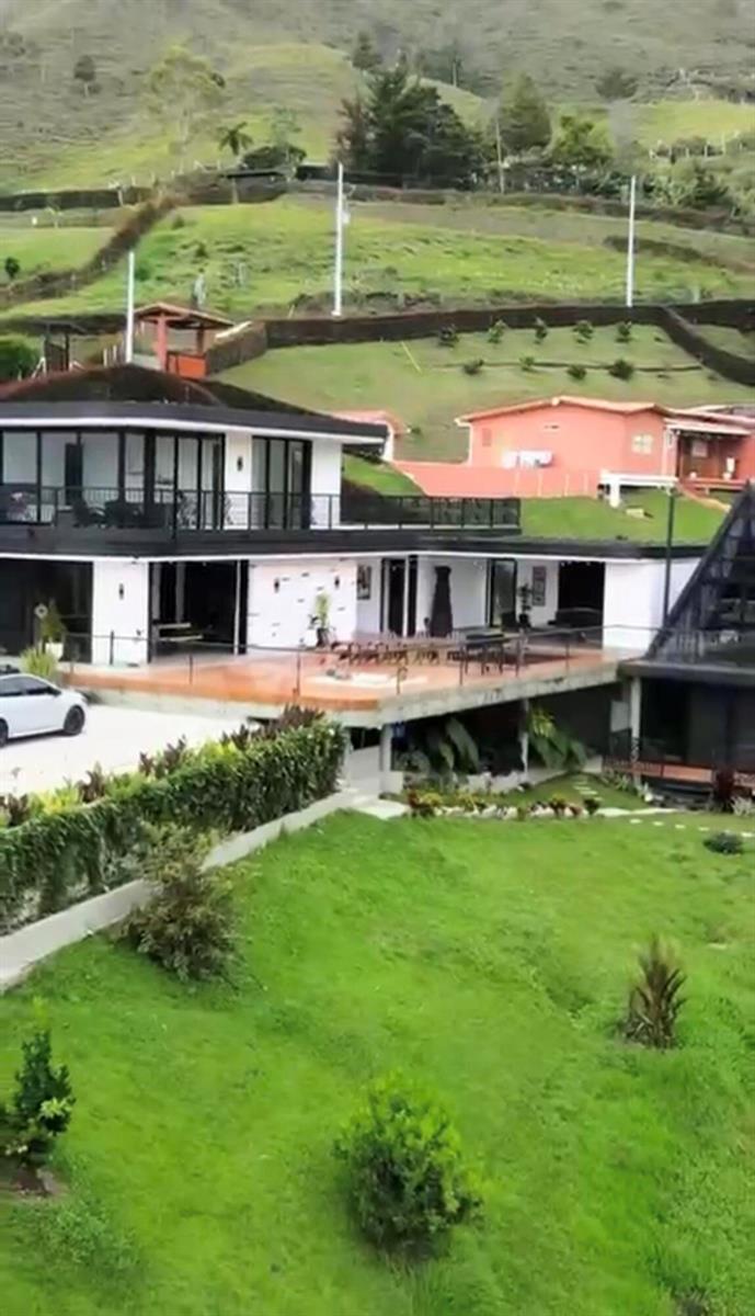 A modern two-story house with a large deck sits on a grassy hillside — Los Altos Del Penol El Penol, FL