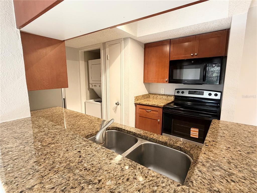 A kitchen features granite countertops, wood cabinets, a black stove, and an adjacent laundry closet — 10200 GANDY BOULEVARD N UNIT 915, ST PETERSBURG, FL