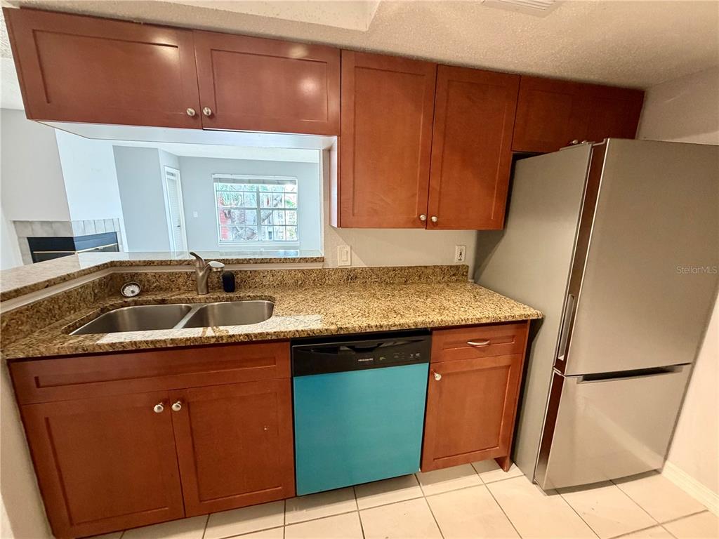 A kitchen features wood cabinets, granite countertops, a stainless steel refrigerator, and a blue dishwasher — 10200 GANDY BOULEVARD N UNIT 915, ST PETERSBURG, FL