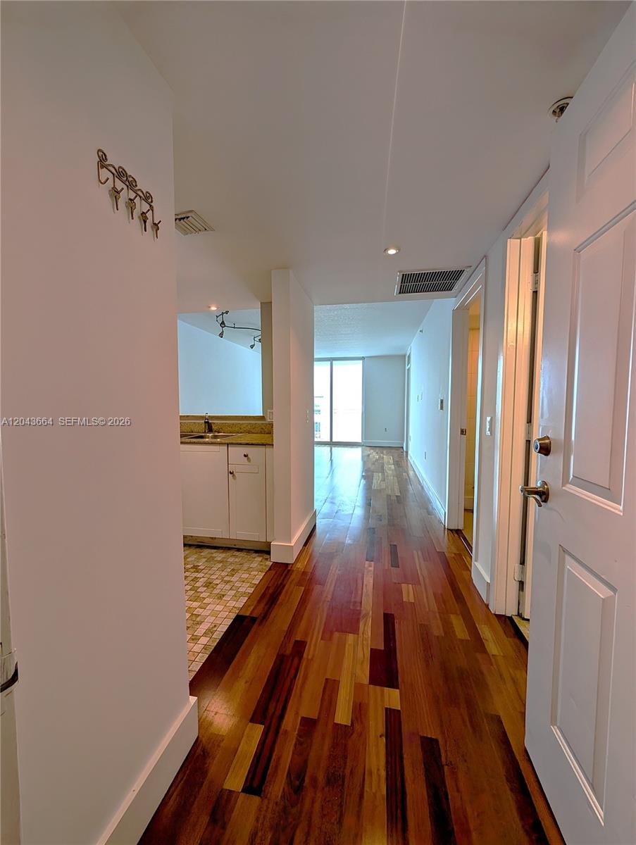 A hallway with hardwood flooring leads to a kitchen and a bright living area — 60 NW 37th Ave # 605, Miami FL 33125, MIAMI, FL