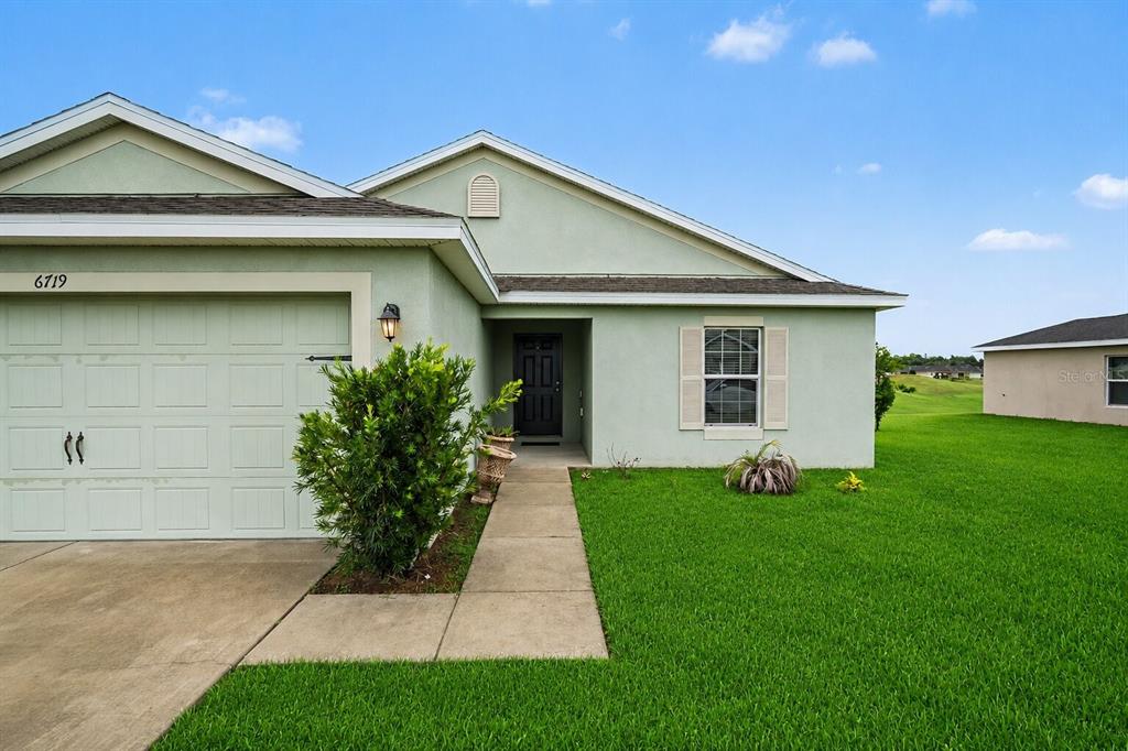 A single-story house with light green stucco, a garage, and a concrete walkway — 6719 WIREVINE DRIVE, BROOKSVILLE, FL