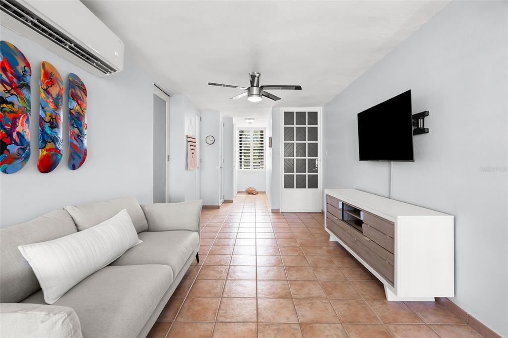 A living room with a gray sofa, tile floors, a ceiling fan, and wall-mounted television — Casa Del Mar II BARRIO MAMEYES UNIT 1806, RIO GRANDE, PR