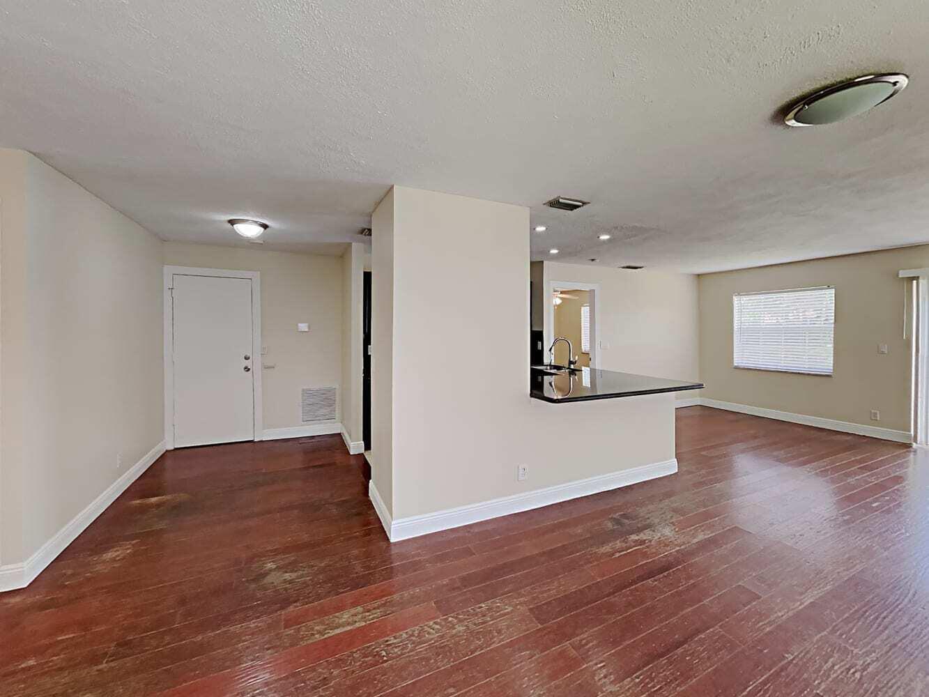 A living area with hardwood floors, a kitchen peninsula, and a white entry door — BOYNTON BEACH, FL