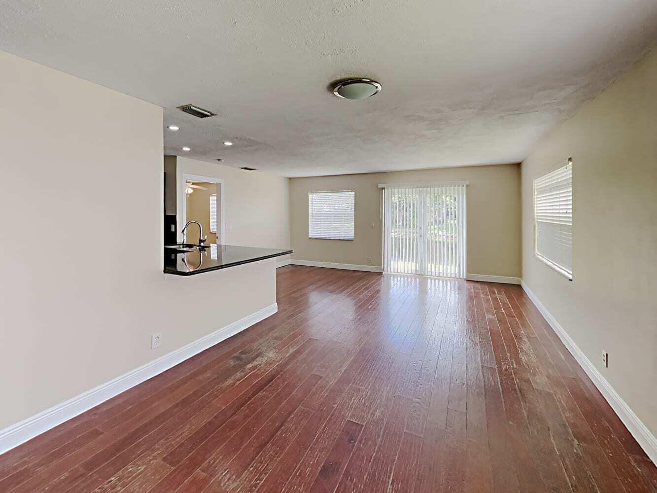 An empty living room with hardwood floors, a kitchen breakfast bar, and sliding glass doors — BOYNTON BEACH, FL