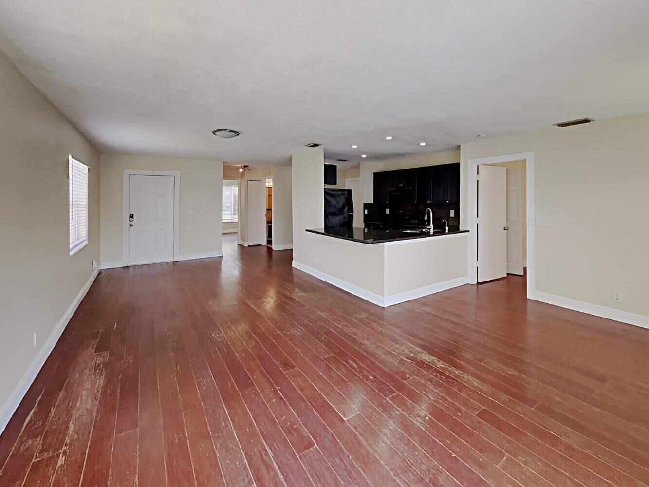 An open-concept living area features hardwood floors, a kitchen with black cabinets, and beige walls — BOYNTON BEACH, FL