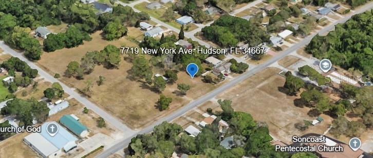 This aerial view shows a vacant lot with scattered trees in a residential neighborhood — 7719 NEW YORK AVENUE, HUDSON, FL