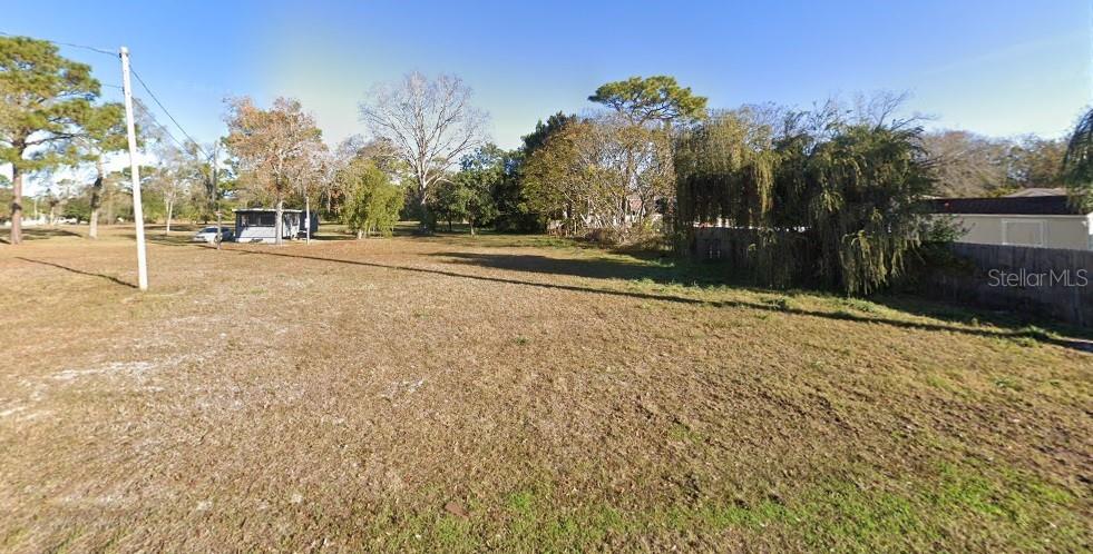 A vacant, grassy lot with scattered trees and a small structure in the background — 7719 NEW YORK AVENUE, HUDSON, FL