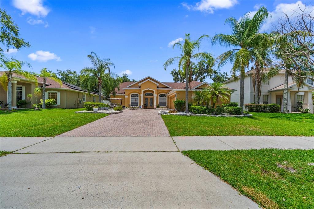 A single-story yellow house with a paved driveway, palm trees, and a green lawn — 2651 RAMBLING OAKS WAY, KISSIMMEE, FL