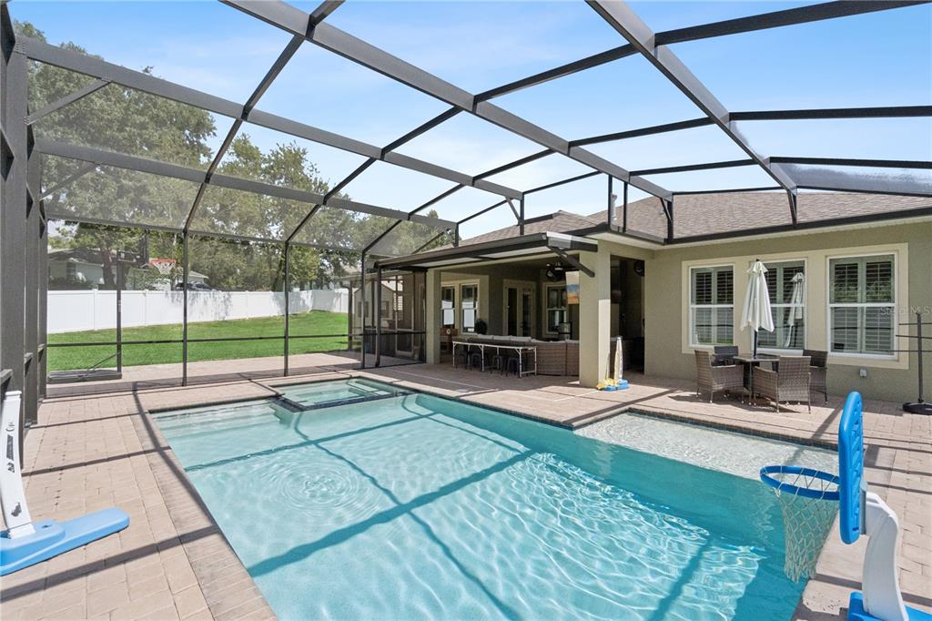 A swimming pool with a spa and basketball hoop sits inside a screened-in patio area — 2336 ZALTANA CIRCLE, MINNEOLA, FL