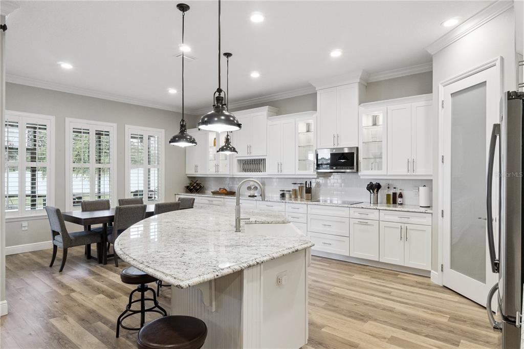 A bright kitchen features white cabinetry, a large granite island, and wood-look flooring — 2336 ZALTANA CIRCLE, MINNEOLA, FL