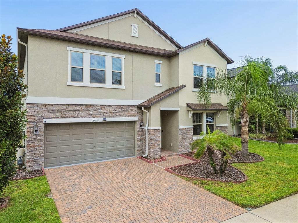 A two-story house with a stone-accented facade, a paved driveway, and a two-car garage — 25057 LAMBRUSCO LOOP, LUTZ, FL