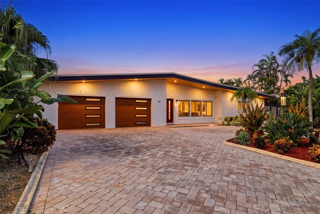 A single-story house with a paved driveway, two wooden garage doors, and tropical landscaping — 661 79TH CIRCLE S, ST PETERSBURG, FL