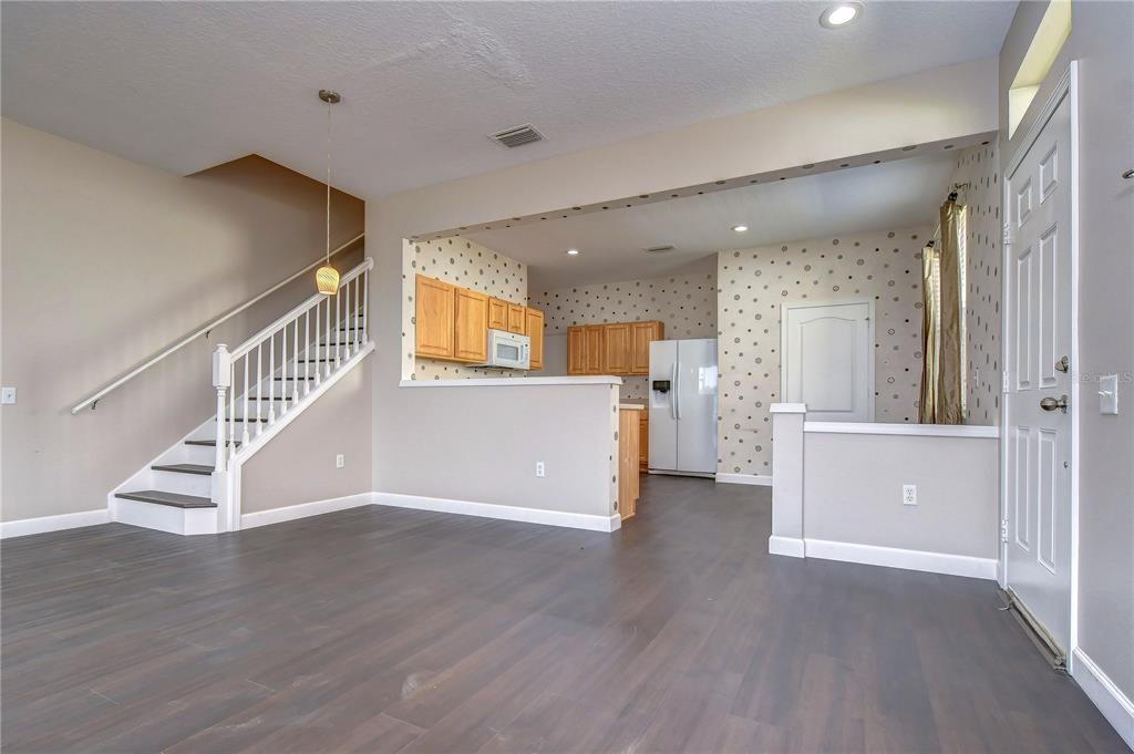 A living area with dark wood floors, a staircase, and an open kitchen with wallpaper — 4744 POND RIDGE DRIVE UNIT 1, RIVERVIEW, FL