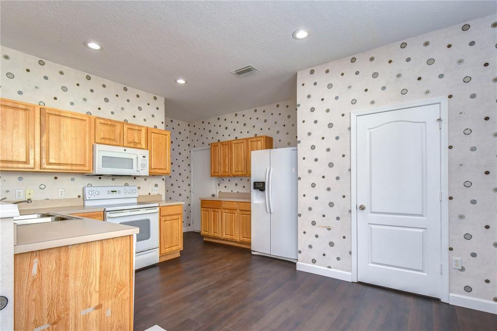 A kitchen features light wood cabinets, white appliances, and walls covered in polka-dot wallpaper — 4744 POND RIDGE DRIVE UNIT 1, RIVERVIEW, FL