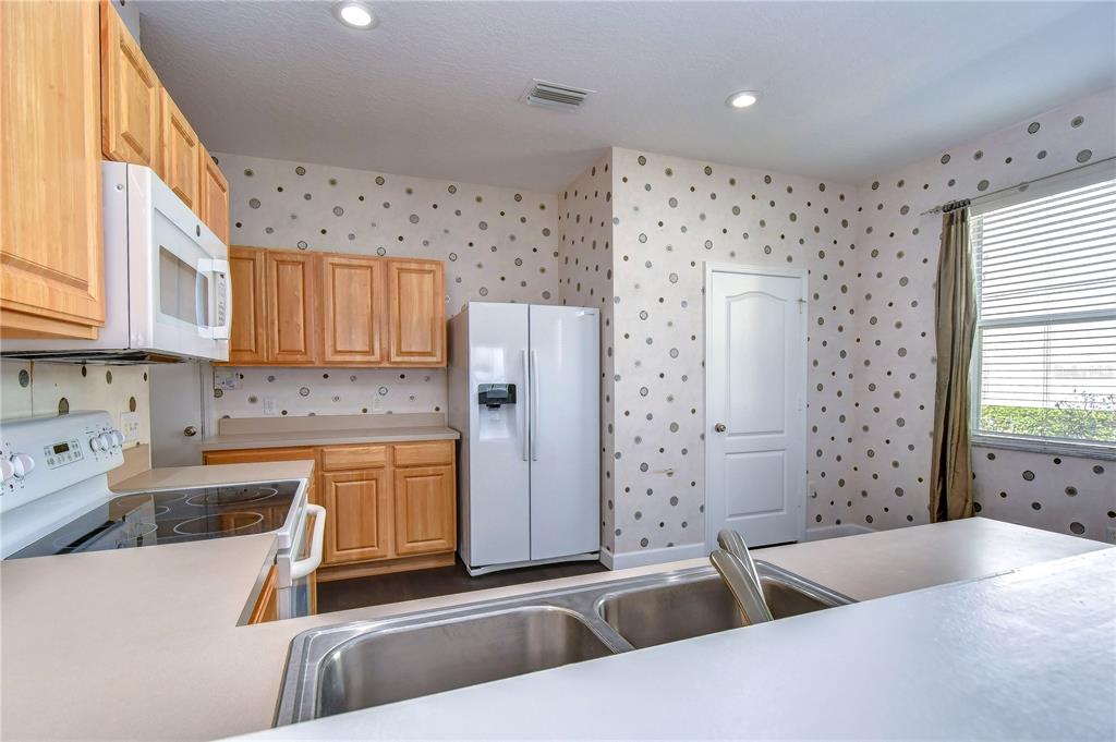 A kitchen features light wood cabinets, a white refrigerator, and polka-dot wallpaper — 4744 POND RIDGE DRIVE UNIT 1, RIVERVIEW, FL