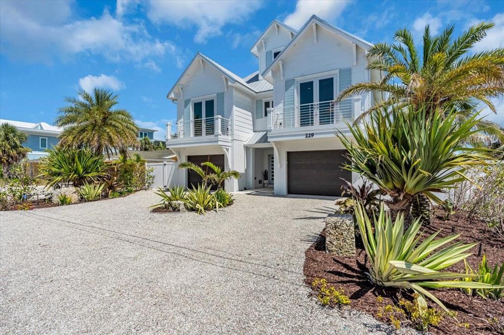A white two-story house with a gravel driveway and tropical landscaping under a blue sky — 229 WILLOW AVENUE, ANNA MARIA, FL