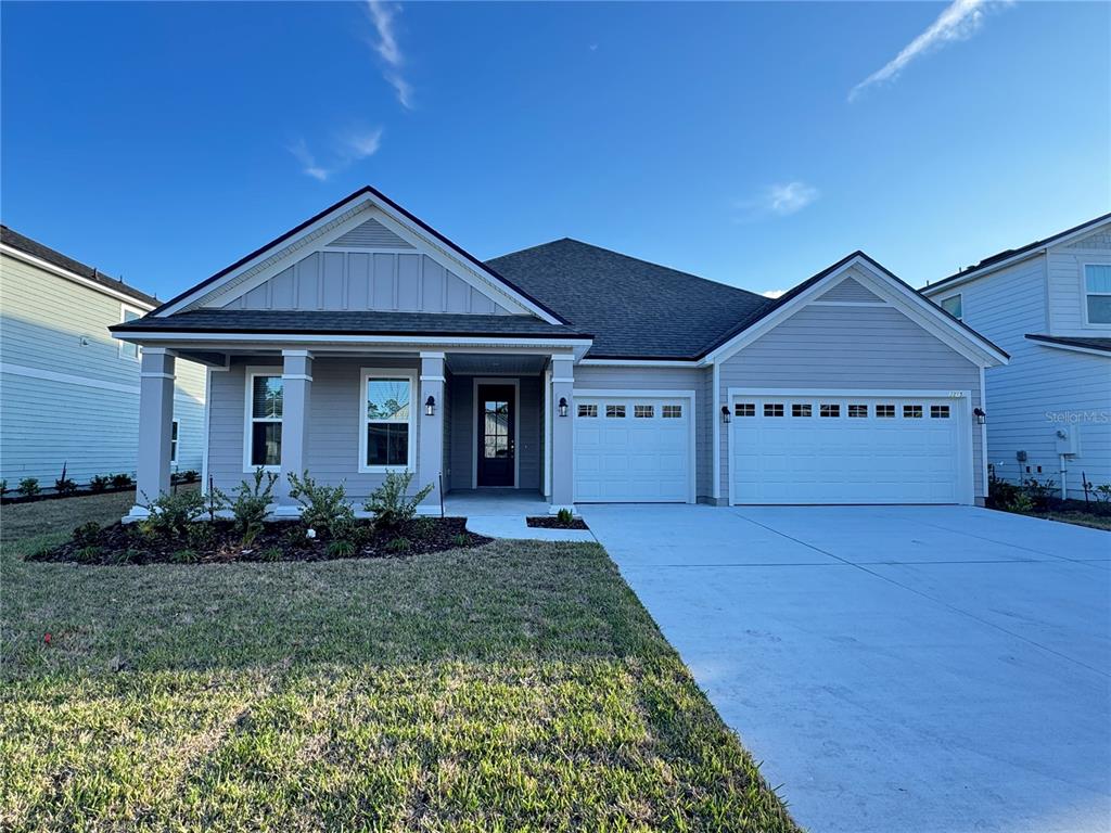 A covered concrete porch features tan horizontal siding, two windows, and a dark front door — 3315 HARVESTERS COURT, GREEN COVE SPRINGS, FL