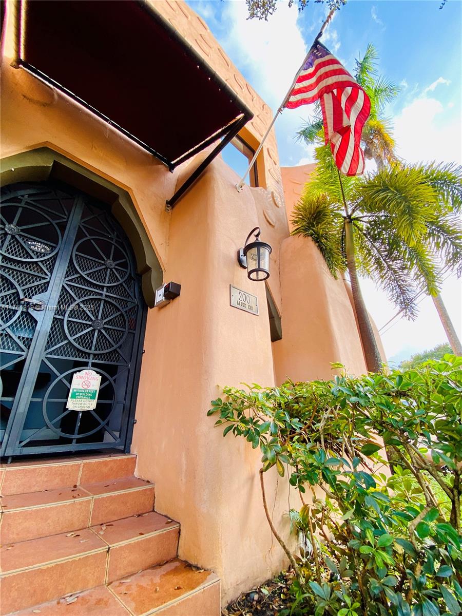 An exterior view shows a peach-colored building entrance with a decorative metal gate and flag — 200 Azure Way, Miami Springs FL 33166, MIAMI SPRINGS, FL