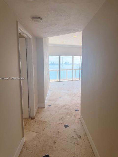 A hallway with light-colored stone tile flooring leads toward a room with floor-to-ceiling windows — 2451 Brickell Ave, Miami FL 33129, MIAMI, FL