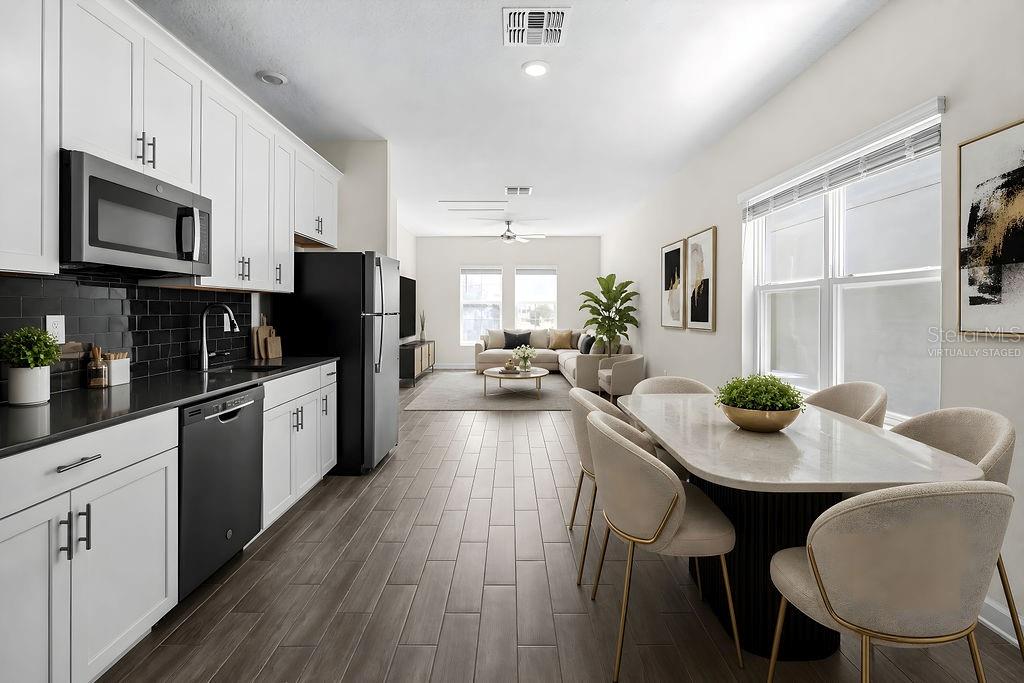 A kitchen with white cabinets and black appliances opens into a dining and living area — 11546 SATIRE STREET, ORLANDO, FL
