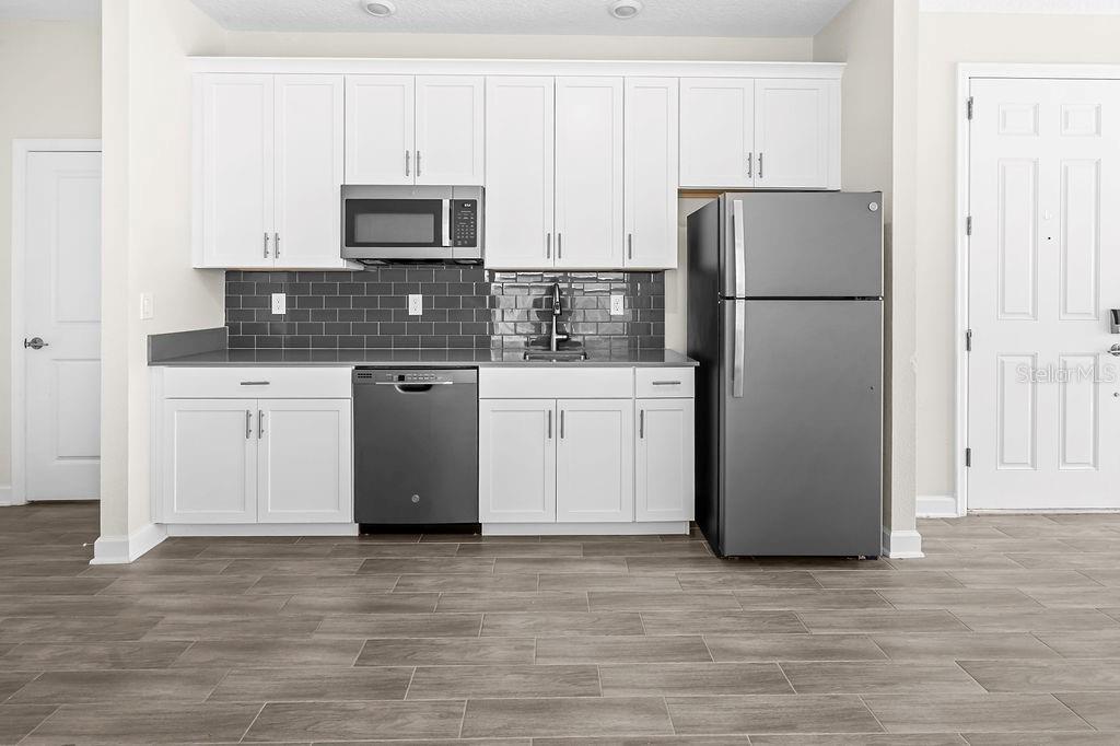 A kitchen with white cabinets, stainless steel appliances, gray tile backsplash, and wood-look tile flooring — 11546 SATIRE STREET, ORLANDO, FL
