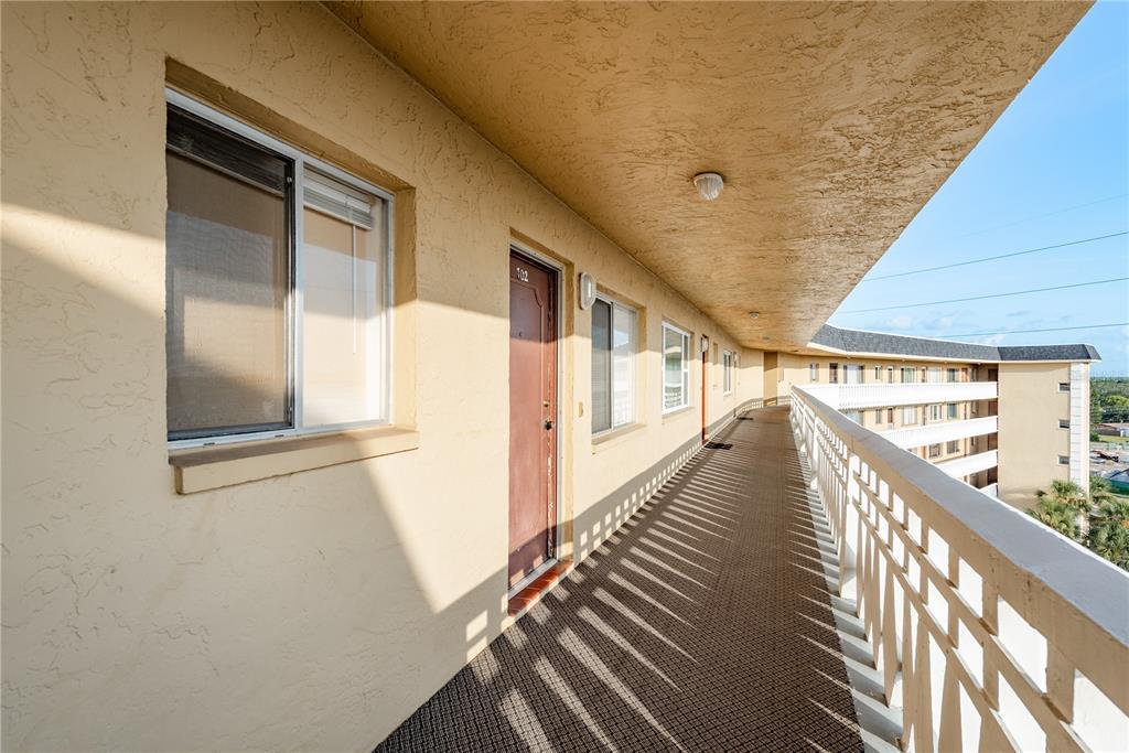 An outdoor apartment building walkway with a brown door, carpeted floor, and white railing — 8950 PARK BOULEVARD UNIT 702, SEMINOLE, FL