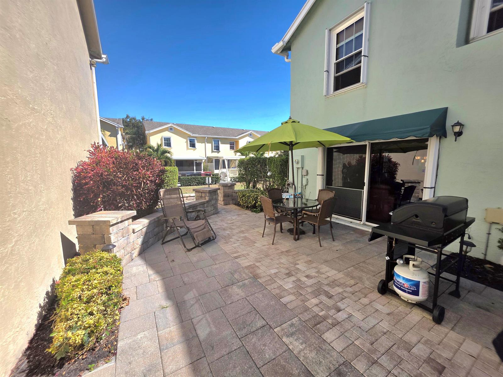 A paved patio features a dining set with a green umbrella and a gas grill — 311 Waterside Drive # 9c, Hypoluxo FL 33462, HYPOLUXO, FL