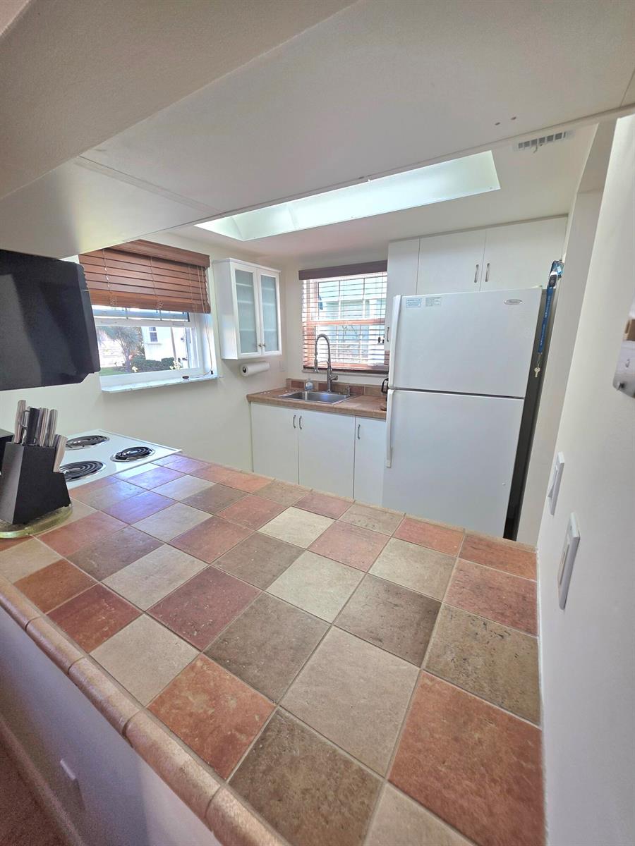 A kitchen features white cabinets, a tiled countertop, a white refrigerator, and a skylight — 311 Waterside Drive # 9c, Hypoluxo FL 33462, HYPOLUXO, FL