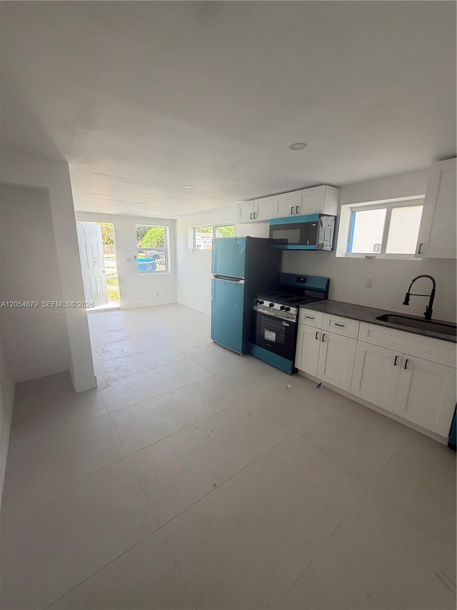A kitchen with white cabinets, dark countertops, and stainless steel appliances opens to a living area — 43 Williams Rd # 3, West Park FL 33023, WEST PARK, FL