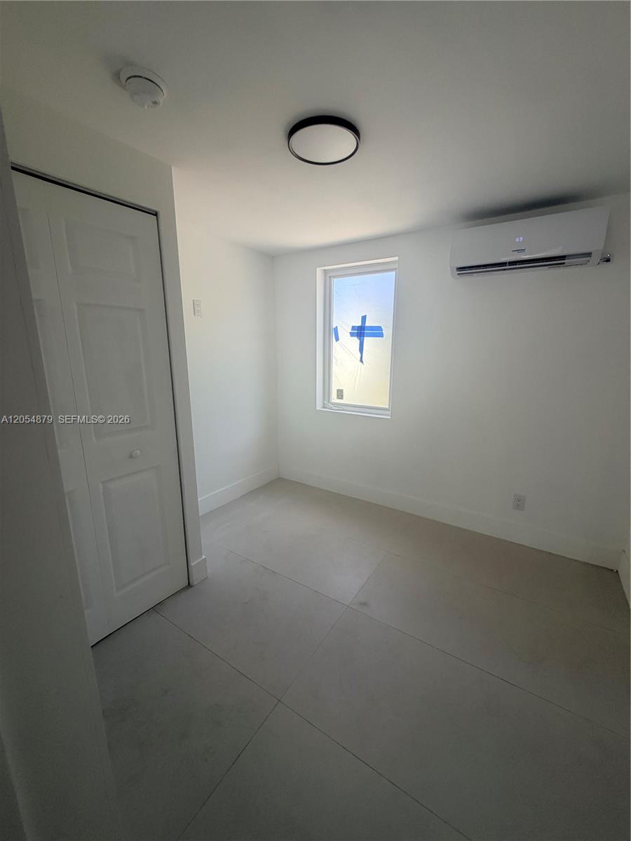 A small, minimalist room features white walls, light tile flooring, a window, and a wall-mounted AC — 43 Williams Rd # 3, West Park FL 33023, WEST PARK, FL