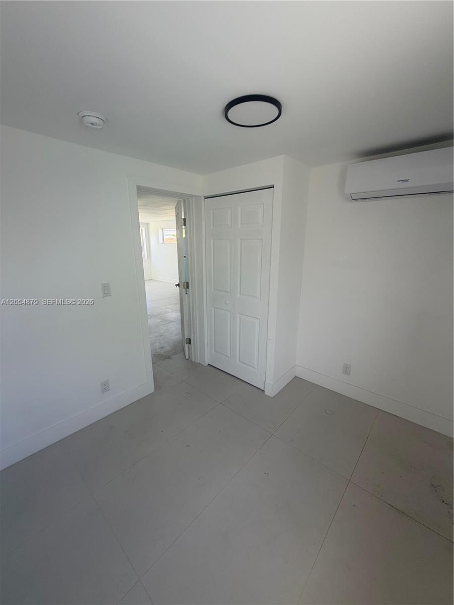 A minimalist room features white walls, light tile flooring, a closet, and a wall-mounted AC unit — 43 Williams Rd # 3, West Park FL 33023, WEST PARK, FL