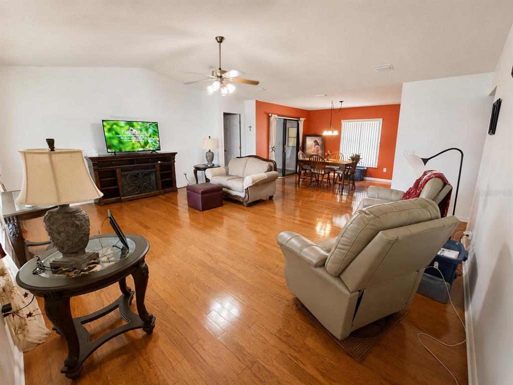 A living room with hardwood floors, a television console, and an adjacent dining area — 4276 SW 140TH STREET ROAD, OCALA, FL