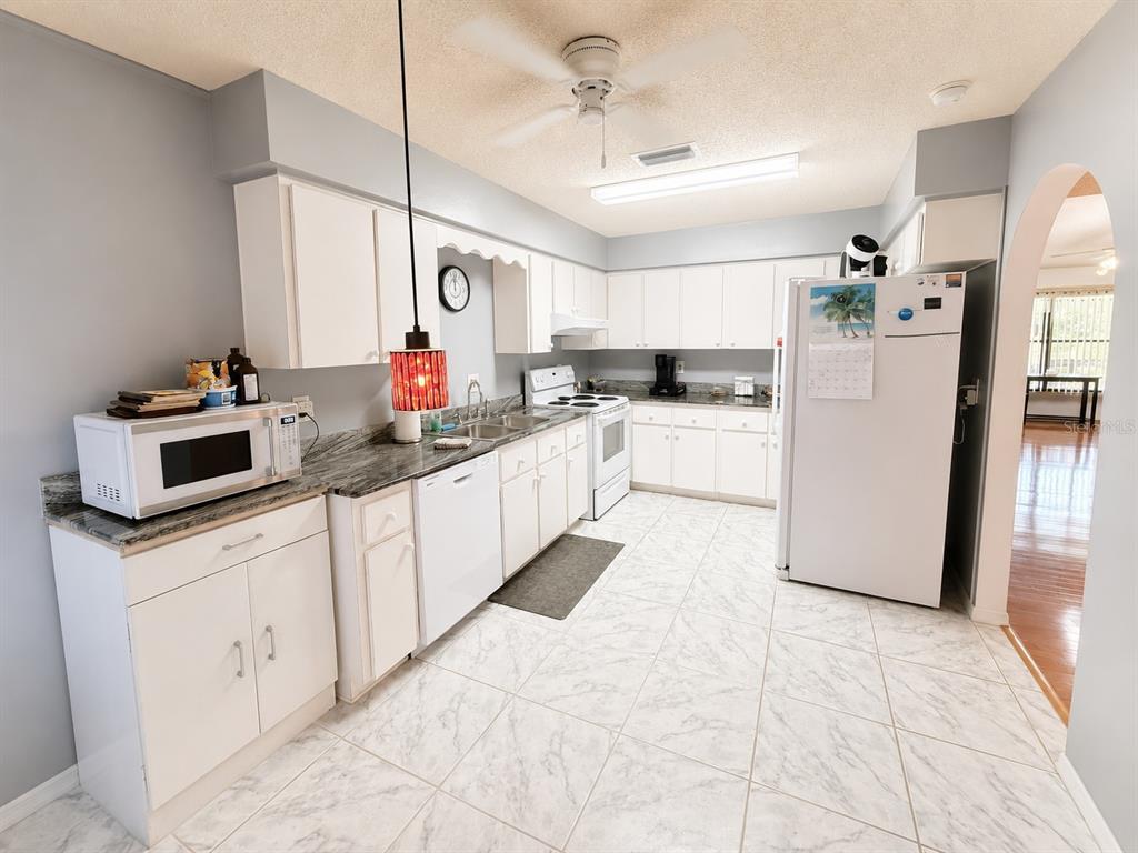 A kitchen features white cabinets, marble-patterned countertops, white appliances, and light-colored tile flooring — 4276 SW 140TH STREET ROAD, OCALA, FL