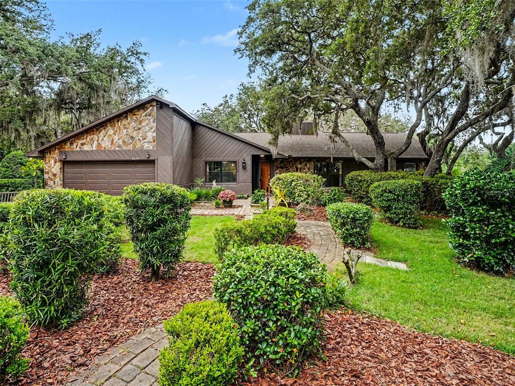 A single-story house with brown siding, stone accents, and a brick walkway surrounded by landscaping — 4870 CITRUS OAK LANE, ST CLOUD, FL